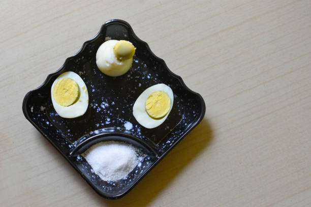 Hard boiled egg cutting in half and salt put on a small black plate isolated white background. Selective focus on sliced egg.