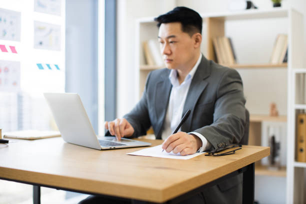 istock Asian businessman in office working on a laptop writing notes 2184270223
