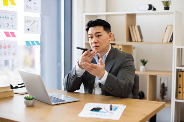 istock Asian businessman recording audio message in modern office setting 2184271384