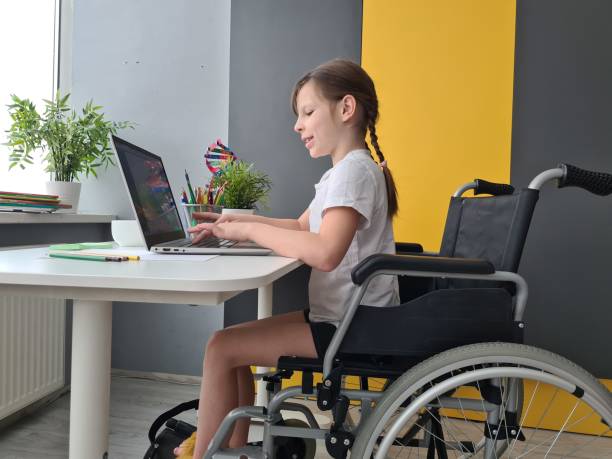 istock Girl in a wheelchair cheerfully using a laptop at a bright workspace 2184276320