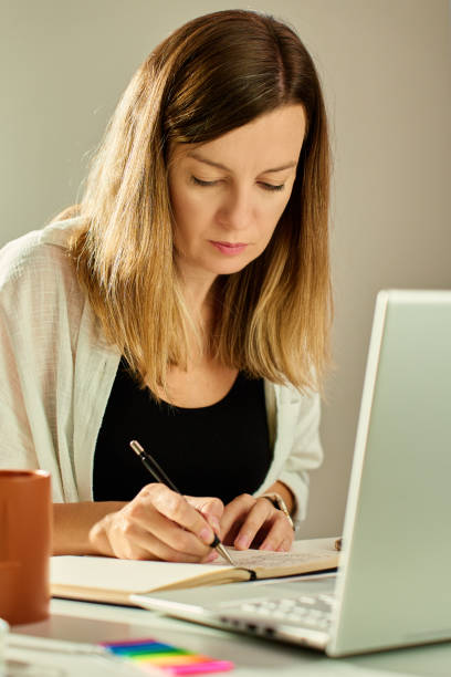 istock Woman working at home, writing in notebook and using laptop 2184278070