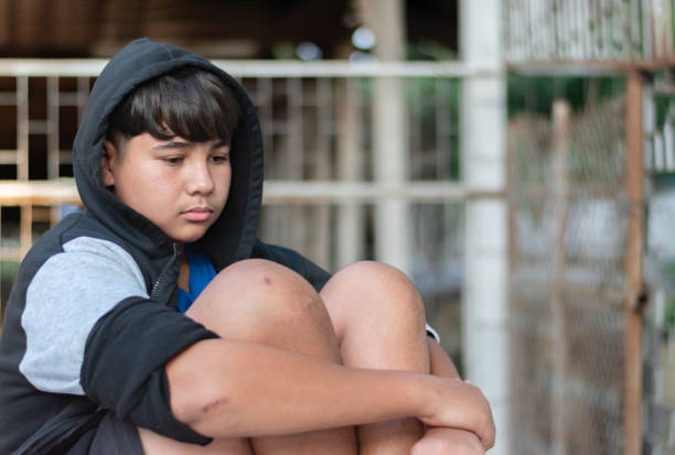 A teenager dressed in shorts and a gray-and-black hooded robe sat secluded in a dirty room, his face gloomy and sad because he was escaping from family problems and punishment from his parents.