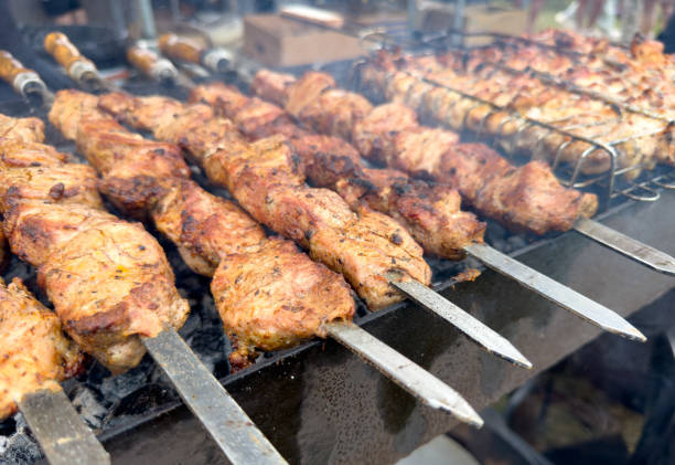 A plate of meat is being cooked on a grill. The meat is being cooked on skewers and is being grilled over an open flame