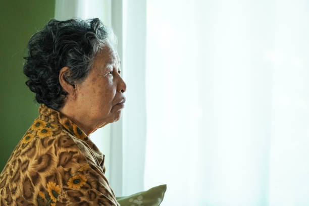 istock Elderly woman sits on a sofa inside a house. 2184286513