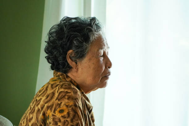 istock Elderly woman sits on a sofa inside a house. 2184286525