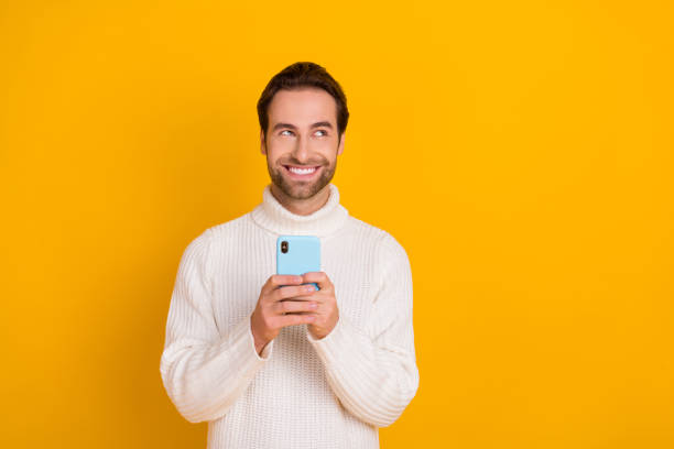 istock Photo of cheerful dreamy guy dressed white sweater writing modern device empty space isolated yellow color background 2184288218