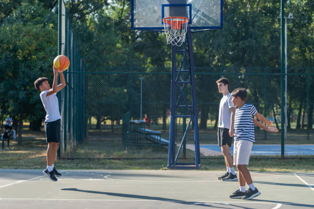 istock Boys engage in outdoor basketball training with a coach, practicing dribbling, passing, and shooting skills on a court surrounded by greenery under bright natural light, fostering teamwork and coordination. 2184293120