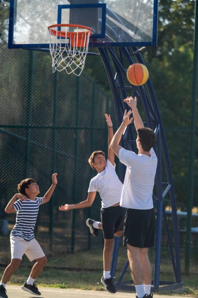 istock Boys engage in outdoor basketball training with a coach, practicing dribbling, passing, and shooting skills on a court surrounded by greenery under bright natural light, fostering teamwork and coordination. 2184293176