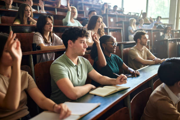istock College students raising hands to express ideas on a class in amphitheater. 2184293697
