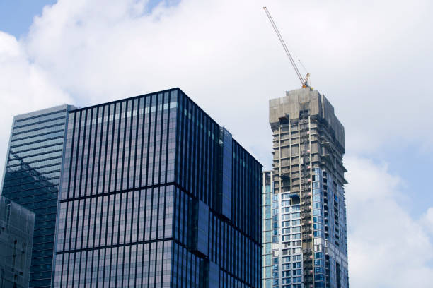 istock Modern Urban Architecture with Construction Crane Against Blue Sky and Clouds Featuring Glass Facades and Steel Structures in a Busy City Environment 2184301311