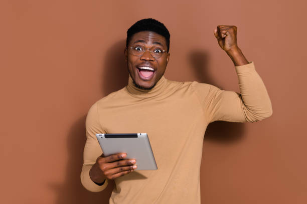istock Portrait of attractive cheerful lucky guy using device web site order rejoicing having fun isolated over brown color background 2184302072