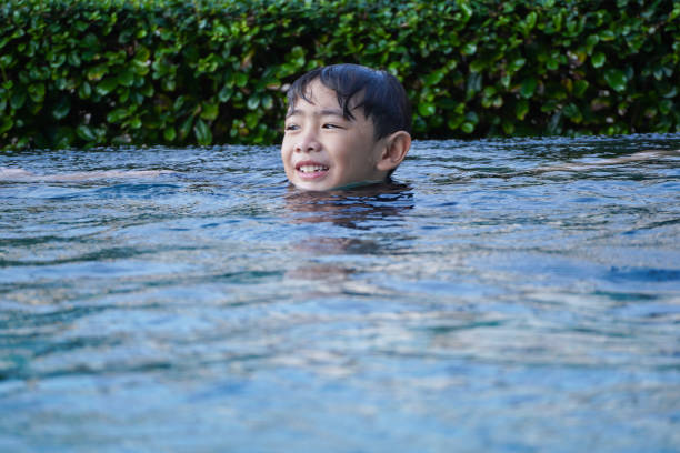 Boy stands in a swimming pool and his head is out of the water.