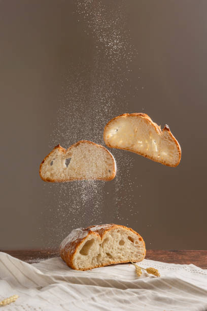 A rustic artisan bread levitates with a sprinkle of flour dust, artistically captured in mid-air, creating a captivating culinary visual against a neutral backdrop.