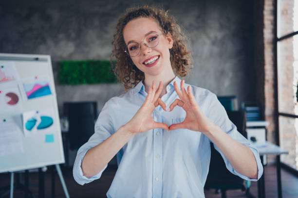 istock Young professional woman forming a heart shape with hands in modern office environment 2184304243