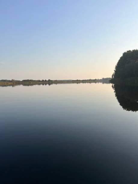 istock Tranquil lake reflecting a clear blue sky and distant tree line at sunrise 2184308406