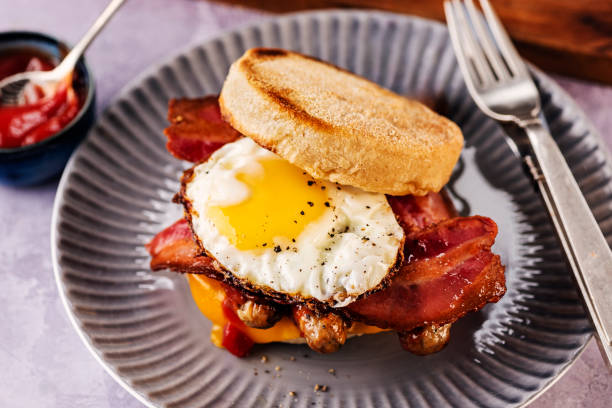 Close-up view of a plate of freshly made English muffin topped with sausages, bacon rashers, a fried egg and melted cheese, a delicious breakfast or brunch. Colour, horizontal format with some copy space. Please see my other pictures in this series for more ideas.