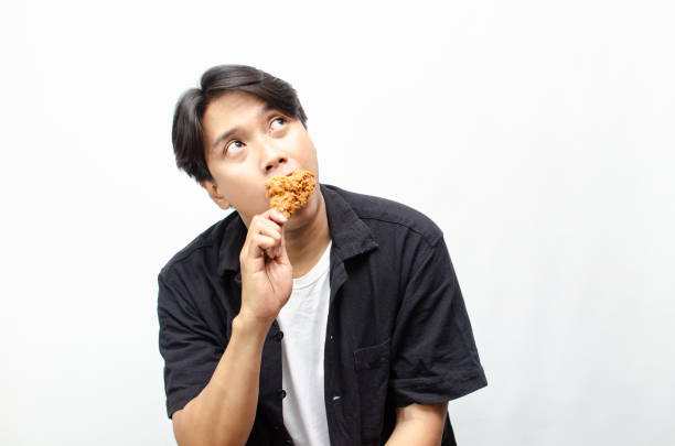 istock Asian Man eating and Biting Crispy Fried Chicken Thigh with a Look of Satisfaction. 2184310131