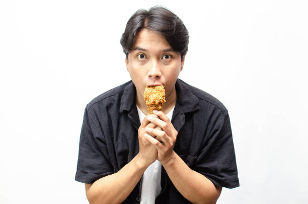 istock Asian Man eating and Biting Crispy Fried Chicken Thigh with a Look of Satisfaction. 2184310134