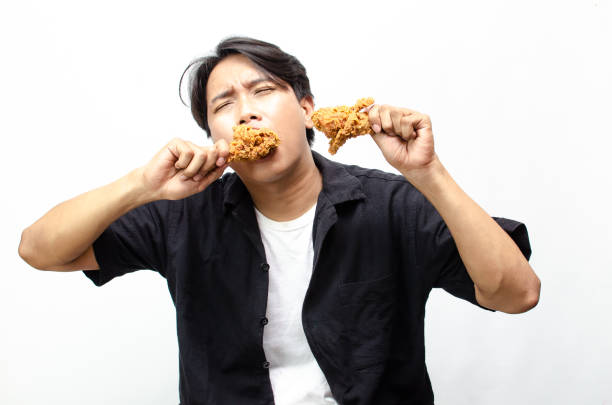 istock Asian Man eating and Biting Crispy Fried Chicken Thigh with a Look of Satisfaction. 2184310152