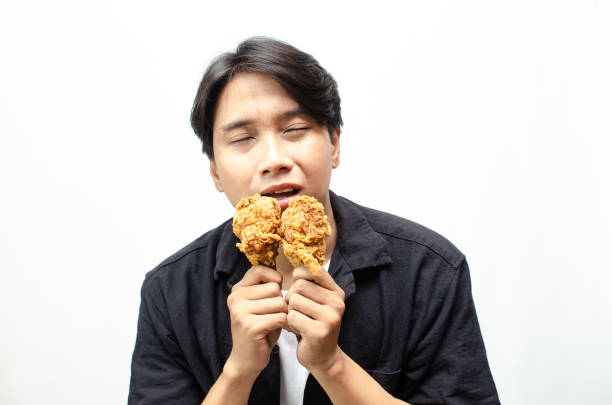istock Asian Man eating and Biting Crispy Fried Chicken Thigh with a Look of Satisfaction. 2184310190