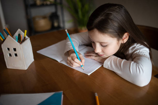 istock child writes with pencil in notebook at home at table. drawing or studying. girl doing homework 2184314944