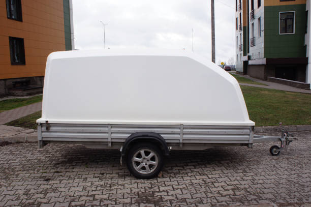 White car trailer covered with plastic lid for transportation and storage. Cargo transportation concept. Trailer standing on the street. Side view.