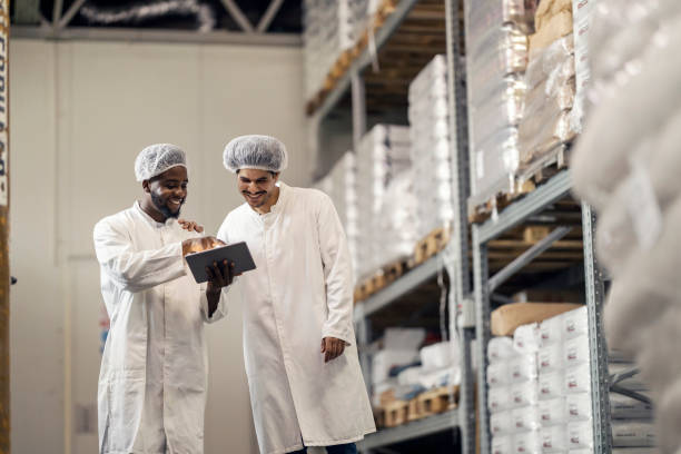 istock Two interracial storage managers and businessmen in uniforms scrolling on tablet at warehouse. 2184333399