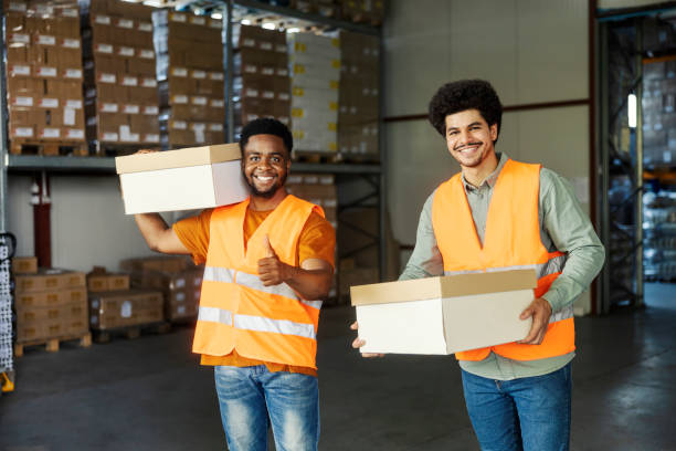 istock Two cheerful hardworking interracial storage workers standing at warehouse with boxes and preparing shipment. 2184333590