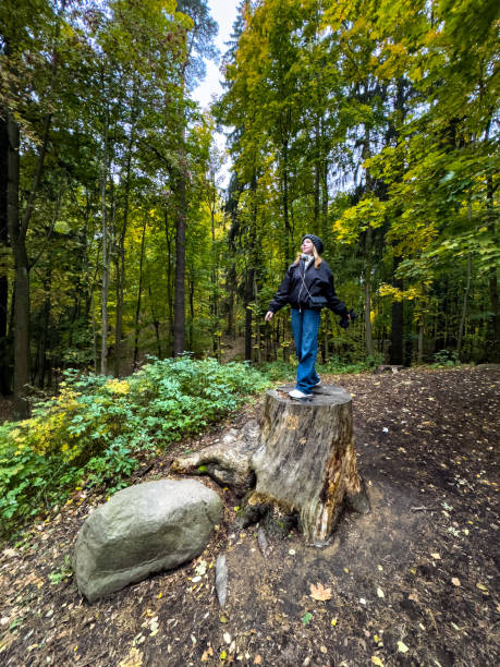 istock Girl Standing on Tree Stump in Autumn Forest, Immersed in Nature 2184333984
