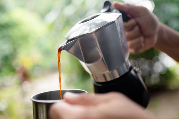 Hand holding a classic moka pot, pouring coffee into a cup.