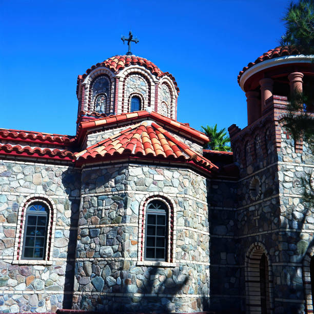 A high-detail shot of a radiant golden Orthodox cross atop the ornate dome of a Byzantine-style temple. The gilded religious symbol stands in sharp contrast against a deep, cloudless blue sky. This architectural detail captures the intersection of Eastern Orthodox tradition and historic Byzantine design. The composition provides clean lines and ample copy space.