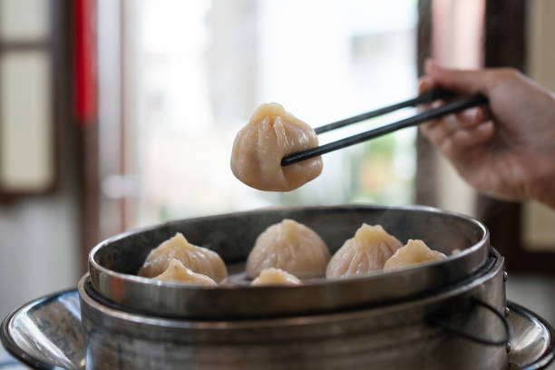 istock Hand using chopsticks to pick up a hot xiao long bao (steamed dumpling) from a steaming plate. 2184339473