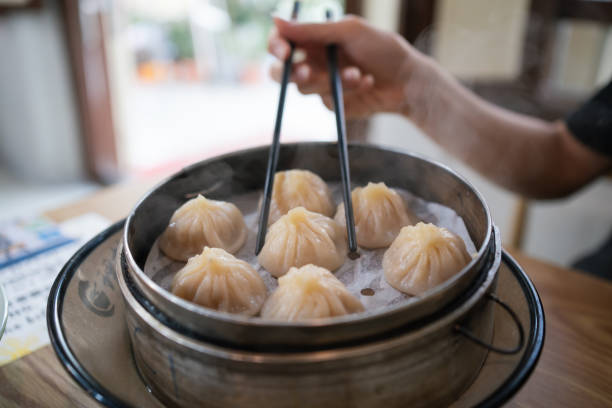 istock Hand using chopsticks to pick up a hot xiao long bao (steamed dumpling) from a steaming plate. 2184339478