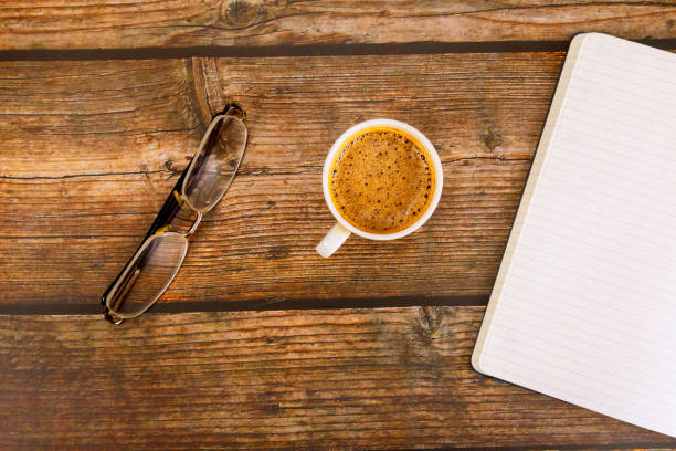 Against wooden background, an open notebook planner sits next coffee espresso.