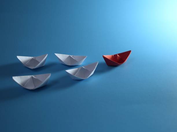 istock Creative idea. Red paper boat navigates among white on blue background 2184352770