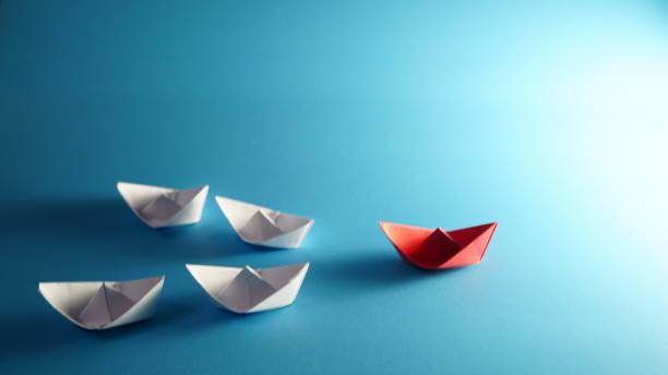 istock Creative idea. Red paper boat navigates among white on blue background 2184352892