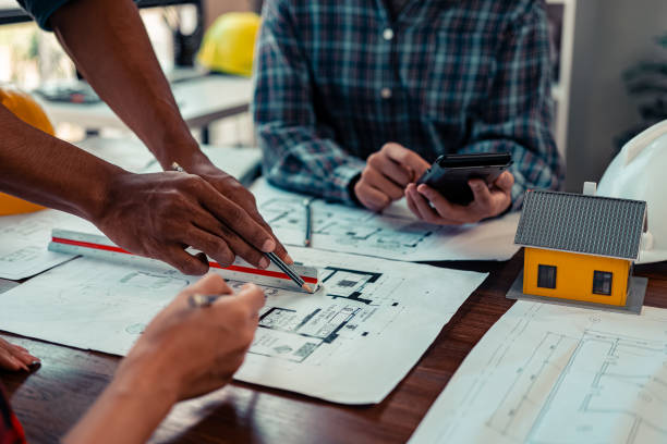istock A team of architects plans and verifies home designs and home models. Architect designs working drawings, plans, blueprints, close-up images. 2184353737