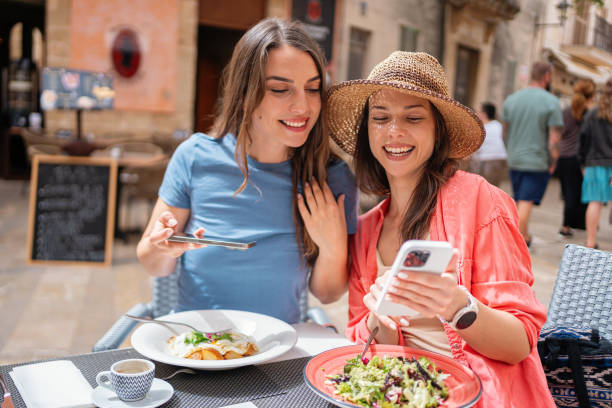 Two female friends sharing a moment and photographing their meals in a sidewalk restaurant in Alcúdia City, Mallorca stock photo
