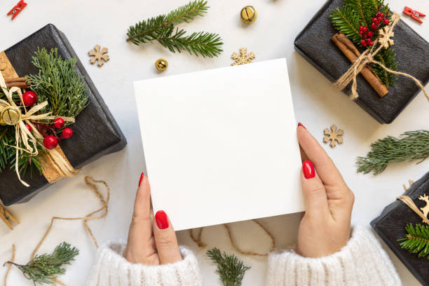 istock Hands with square card near gift boxes, fir branches and Christmas decor, Mockup 2184354336