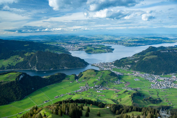 A sweeping panoramic view from the summit of Stanserhorn, featuring the tranquil Lake Lucerne surrounded by forested hills and green meadows at the mountains base. This scenic vista highlights the beauty of Switzerland lush landscapes, where alpine nature meets picturesque valleys and open fields.