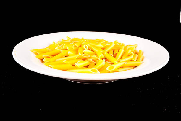 A plate of pasta is sitting on a black background. The pasta is yellow and he is cooked
