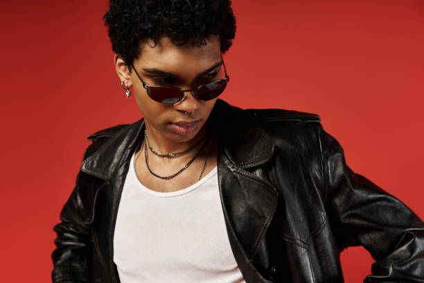 istock Stylish man wearing sunglasses strikes a confident pose against a vibrant red backdrop 2184365684