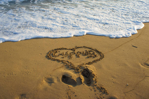 istock Simple heart drawn in sand on a sunny beach with gentle waves lapping at the shore. 2184366564