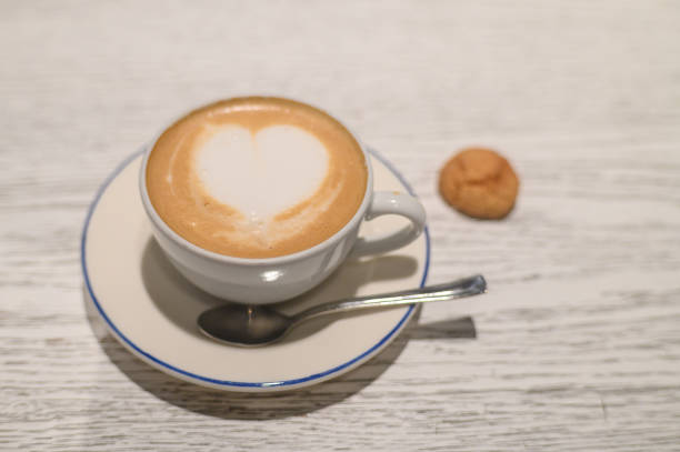 Delightful coffee with heart-shaped froth accompanied by a cookie on a rustic wooden table