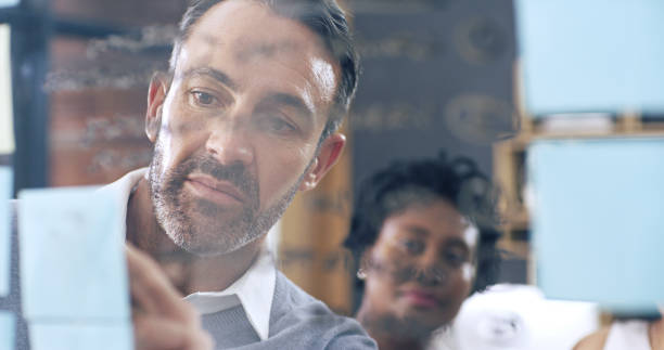 istock Man, meeting and glass wall for sticky notes, thinking and erp discussion with report. Office, brainstorming and workshop for small business, teamwork and partnership collaboration or b2b project 2184371318