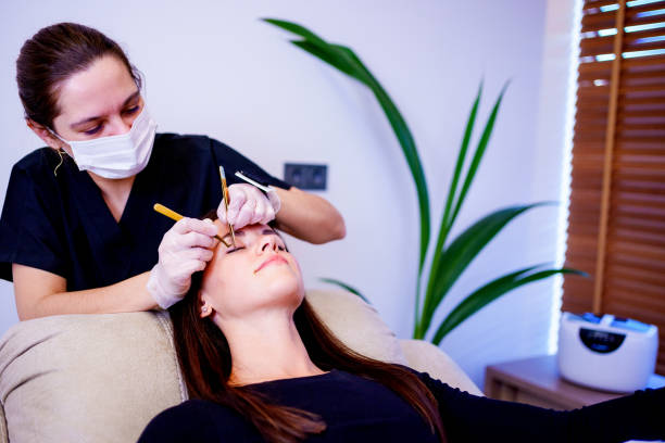 A beautician applies artificial eyelashes to a client in a beauty salon with work tools in her hands, the concept of beauty treatment Woman Eye with Long Eyelashes. Beauty treatment, applying false eyelashes