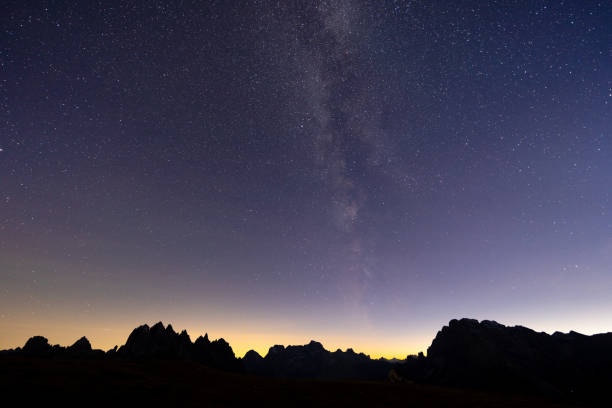 many stars and milkyway on night sky over silhouette of mountains in the dolomites, italy in late autumn season