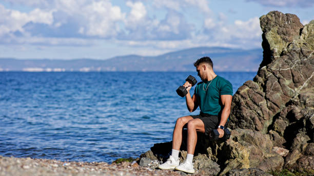 istock Young Man Performing Dumbbell Tricep Kickback Exercise on Rocky Coastline with Sea Background 2184387307