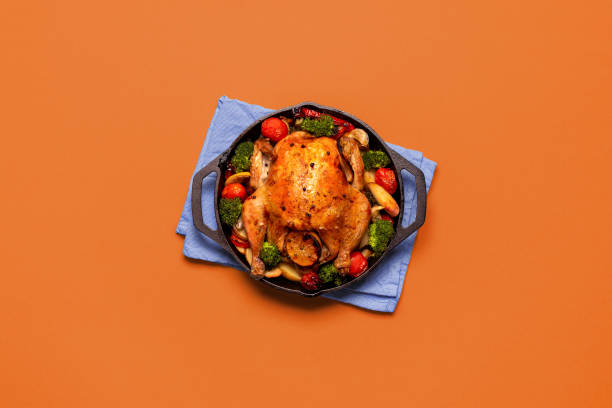 istock Roasted chicken with vegetables in an iron cast, isolated on an orange background. 2184389810