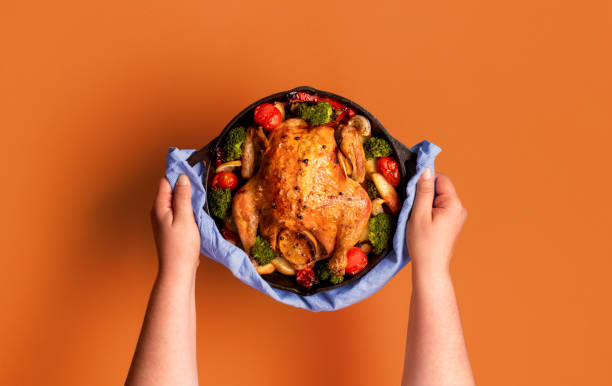 Roasted chicken in an iron cast, with vegetables, minimalist on an orange background.